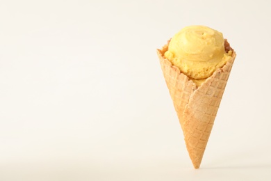 Delicious yellow ice cream in waffle cone on white background. Space for text