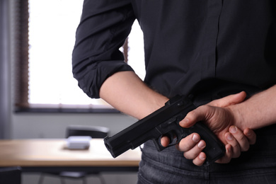 Man holding gun indoors, closeup. Dangerous criminal