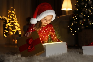 Cute little girl opening gift box in room decorated for Christmas