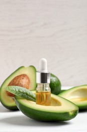 Essential oil and avocados on white table. Space for text
