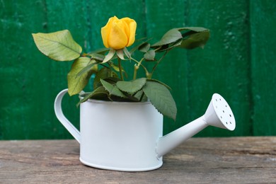 Photo of Stylish watering can with beautiful rose on wooden table