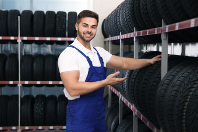 Male mechanic near rack with car tires in auto store
