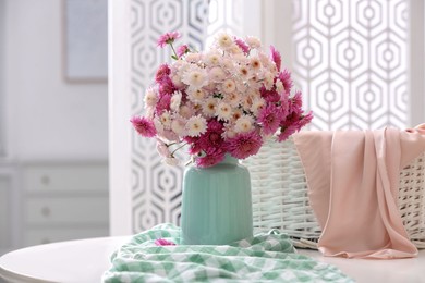Vase with beautiful bouquet, wicker basket and checkered cloth on white table in room