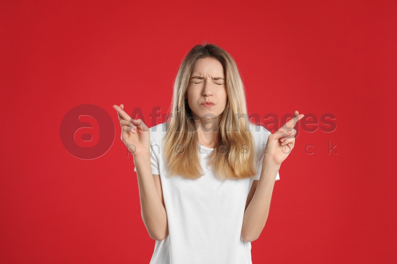 Woman with crossed fingers on red background. Superstition concept