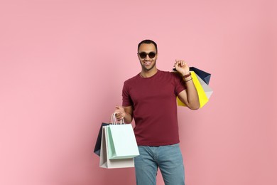 Photo of Happy African American man in sunglasses with shopping bags on pink background