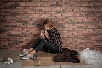Poor homeless woman eating on floor near brick wall