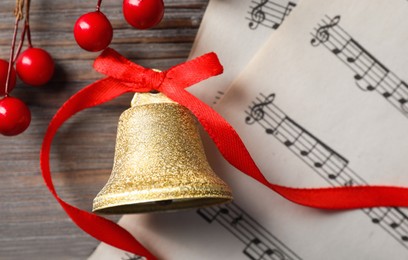 Photo of Golden shiny bell with red bow, music sheets and decorative branch on wooden table, flat lay. Christmas decoration