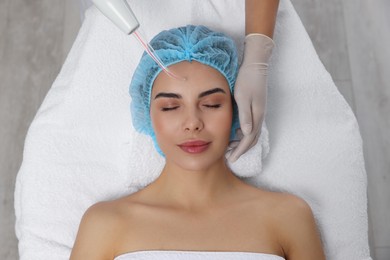 Young woman undergoing face rejuvenation procedure with darsonval in salon, top view