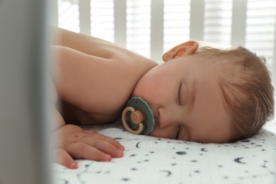 Cute little baby with pacifier sleeping in crib, closeup