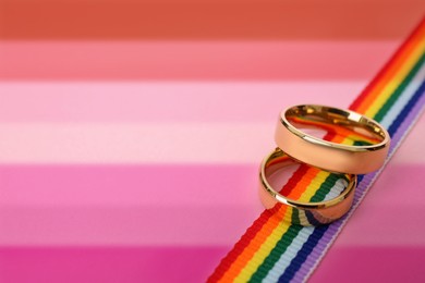 Golden wedding rings and rainbow ribbon on background in color of lesbian flag, space for text.