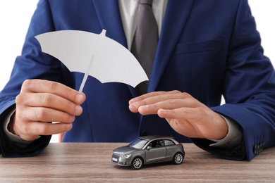 Insurance agent covering toy car with paper cutout umbrella and hand at table, closeup