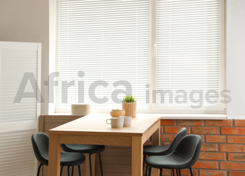 Stylish dining room interior with modern table set and window blinds