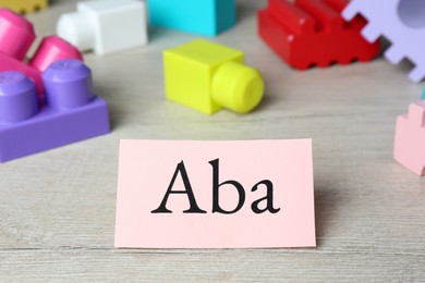Paper sheet with abbreviation ABA (Applied behavior analysis) and colorful wooden blocks on white table, closeup
