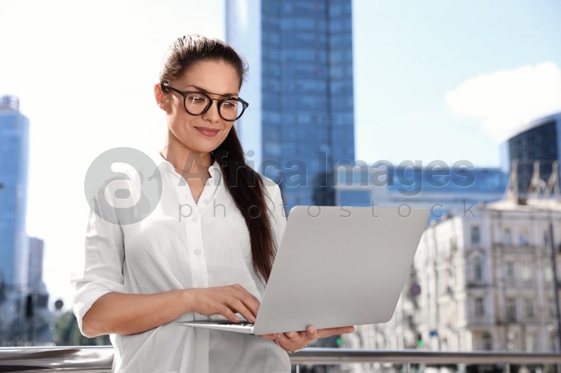 Beautiful businesswoman with laptop on city street