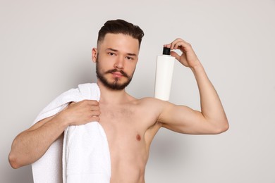 Naked man with towel and bottle of shampoo on light grey background