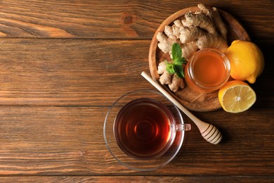 Photo of Cup of delicious ginger tea, honey and lemons on wooden table, flat lay. Space for text