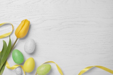 Photo of Flat lay composition with festively decorated Easter eggs and beautiful tulip on white wooden background. Space for text