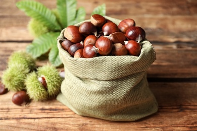 Photo of Fresh sweet edible chestnuts in sack on wooden table