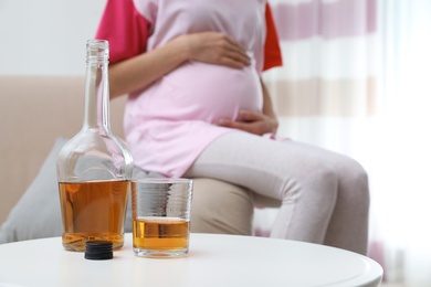 Future mother at home, focus on bottle and glass with alcohol drink. Bad habits during pregnancy