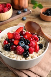 Photo of Bowl with tasty oatmeal porridge and berries served on wooden table. Healthy meal