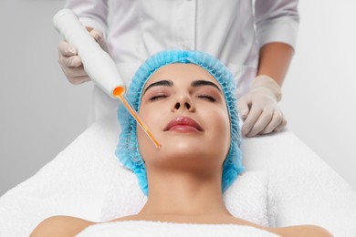 Young woman undergoing face rejuvenation procedure with darsonval in salon