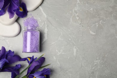 Jar with purple sea salt, spa stones and beautiful flowers on grey marble table, flat lay. Space for text