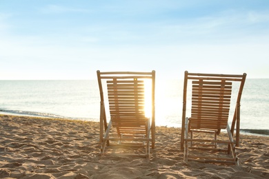 Photo of Wooden deck chairs on sandy beach. Summer vacation