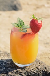 Glass of refreshing drink with strawberry and mint on rock outdoors