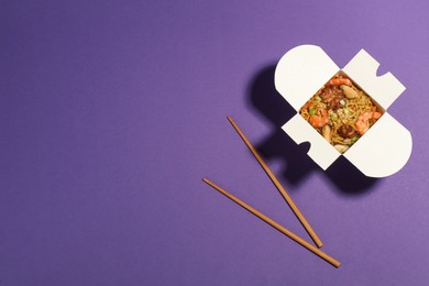 Noodle wok with chopsticks on purple background, flat lay. Space for text