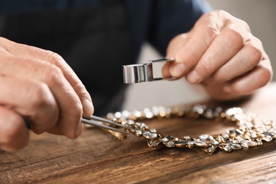 Male jeweler evaluating necklace at table in workshop, closeup