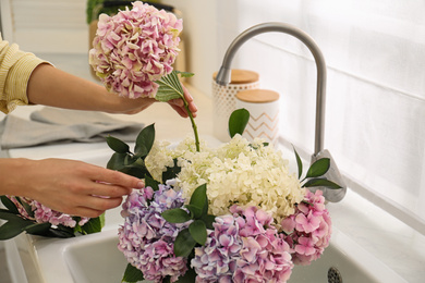 Woman making bouquet with beautiful hydrangea flowers in kitchen, closeup