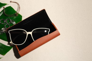 Flat lay composition with stylish sunglasses and brown leather case on sand. Space for text
