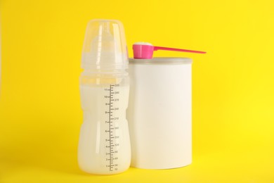 Blank can of powdered infant formula with feeding bottle and scoop on yellow background. Baby milk