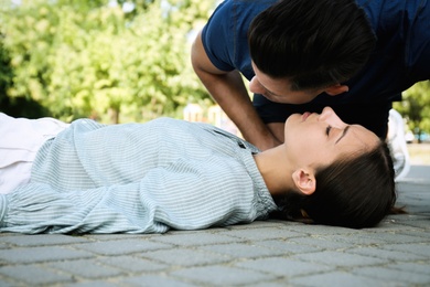 Man checking for breathing of unconscious young woman outdoors