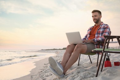 Man using laptop in camping chair on sandy beach