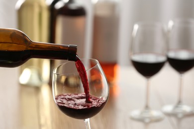 Pouring red wine from bottle into glass on blurred background, closeup. Space for text
