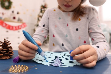 Little child making Christmas craft at blue wooden table in decorated room, closeup