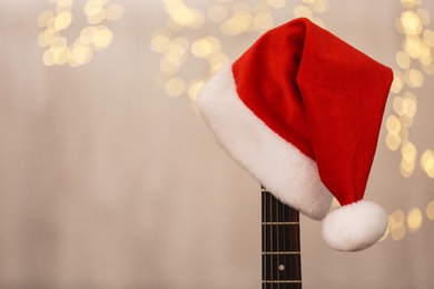 Guitar with Santa hat against blurred lights, space for text. Christmas music