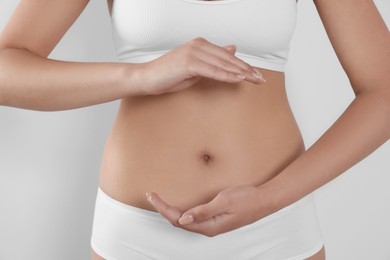 Photo of Woman in underwear holding something near her belly on light background, closeup. Healthy stomach