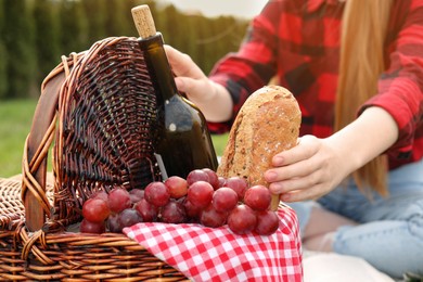 Girl taking bread from wicker picnic basket outdoors, closeup