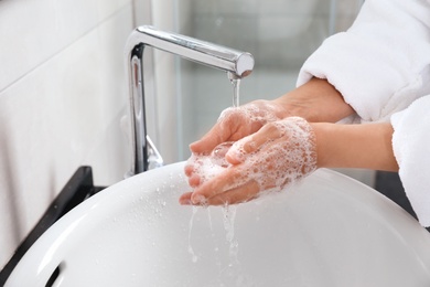 Woman washing hands with soap over sink in bathroom, closeup