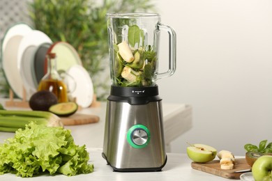 Photo of Blender with ingredients for green smoothie on white wooden table in kitchen