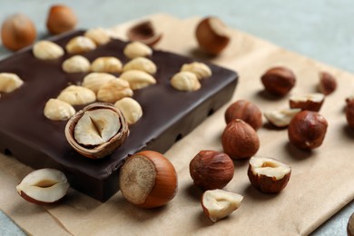 Delicious chocolate bar and hazelnuts on parchment paper, closeup