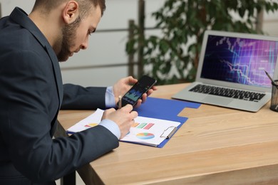 Forex trader working with smartphone and charts at table in office