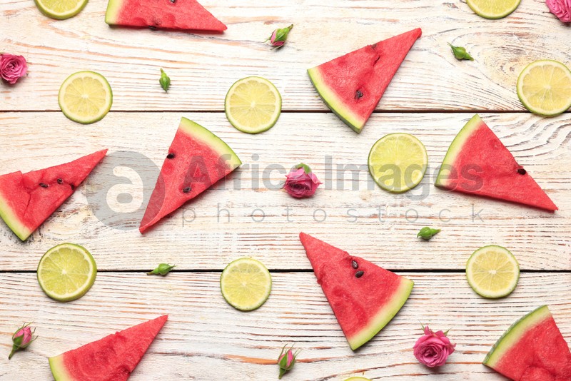 Tasty sliced watermelon, roses and limes on white wooden table, flat lay