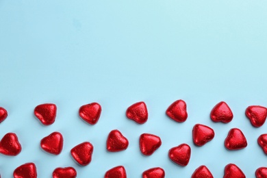 Heart shaped chocolate candies in red foil on light blue background, flat lay. Space for text