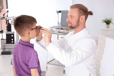 Children's doctor putting glasses on little boy in clinic
