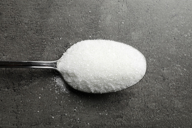 Photo of Spoon of white sugar on grey table, top view