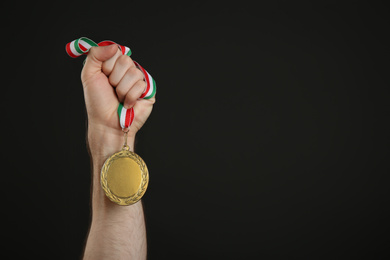Man holding golden medal on black background, closeup. Space for design