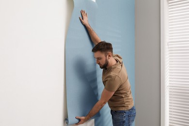 Man hanging stylish wall paper sheet indoors
